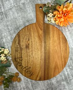 a wooden cutting board sitting on top of a table next to some flowers and an orange flower