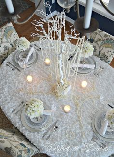 a dining room table is decorated with white flowers and candles for an elegant centerpiece