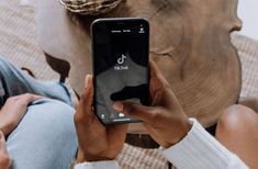 a person holding a cell phone in their hand and sitting on the ground next to an elephant