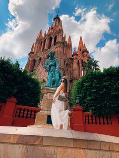 a woman is sitting on the edge of a wall in front of a building with a statue