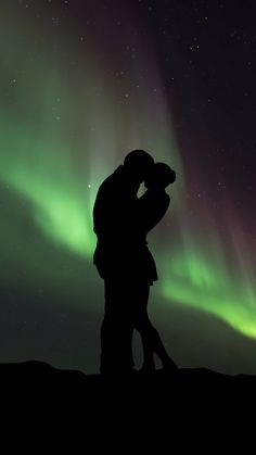 two people are kissing in front of the aurora lights