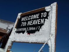 a sign that is covered in snow on the side of a building with a sky background