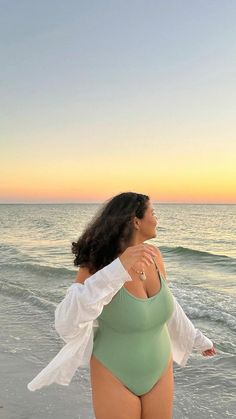 a woman standing on top of a sandy beach next to the ocean wearing a green bodysuit