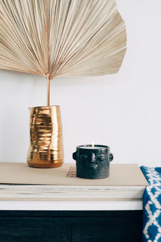 a gold vase sitting on top of a dresser next to a blue and white pillow