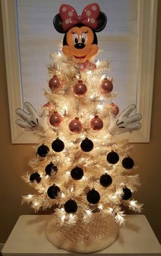 a white christmas tree with minnie mouse decorations on top and lights in the shape of balls