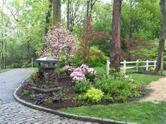 a garden with flowers and trees in the middle of it on a cobblestone path