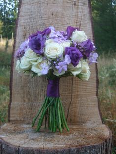 a bouquet of white and purple flowers sitting on top of a tree stump