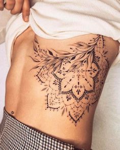 a woman's lower back tattoo with flowers and leaves on her stomach, which is covered in black ink