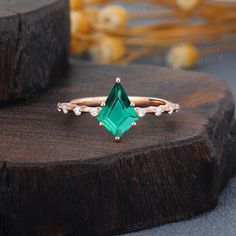 an emerald and diamond ring sitting on top of a piece of wood