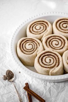 cinnamon rolls in a white bowl with cinnamon sticks next to it