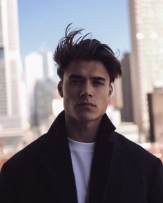 a young man standing in front of a cityscape with his hair blowing in the wind