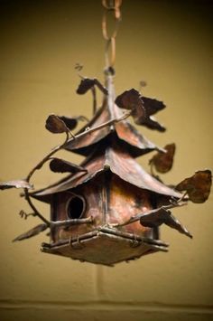 a metal birdhouse hanging from a chain with leaves on it's roof and branches attached to the ceiling