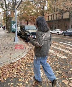 a woman walking down the street with her cell phone in her hand and cars parked on the side of the road