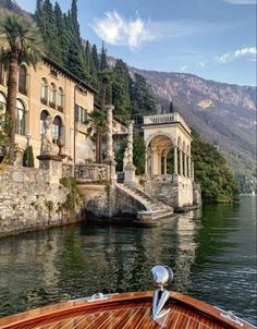 a boat traveling down a river next to a large building on the side of a mountain