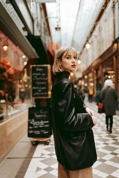 a woman is standing in an indoor shopping mall with her hand on her hip and looking off into the distance