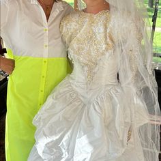 two people dressed up in wedding attire posing for a photo with an umbrella behind them