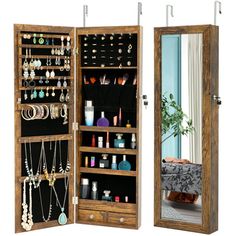 an open wooden jewelry cabinet next to a mirror with necklaces hanging on the doors