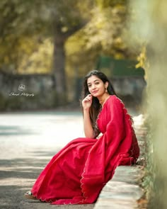 a woman in a red dress sitting on the side of a road with her hand under her chin