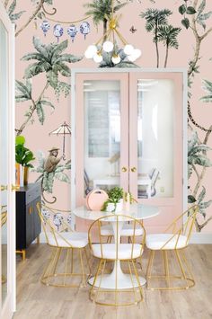 a dining room with pink walls and palm trees on the wall, gold chairs and table