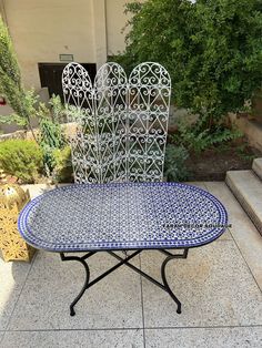 a blue and white table sitting on top of a tiled floor next to some bushes