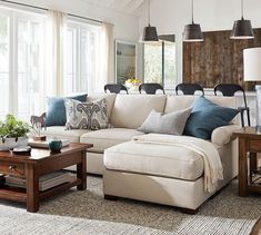 a living room with white couches and blue pillows on top of the sofas