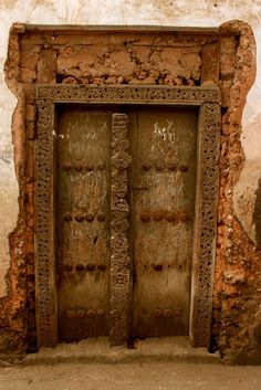 an old door with carvings on it in a stone wall and dirt flooring area