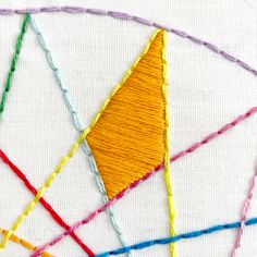 a close up of a piece of art with some thread on the bottom and an orange triangle in the middle