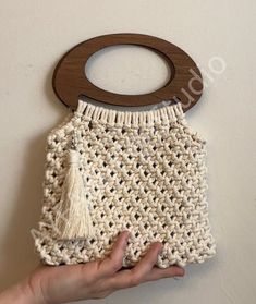 a hand holding a crocheted purse with a wooden hanger attached to it