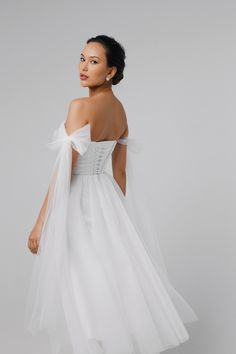 a woman wearing a white wedding dress with an off the shoulder bow at the back