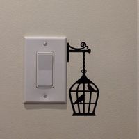 a light switch with a bird in a cage on it's side and a wall sticker