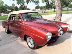 an old red car is parked on the side of the road in front of a tree