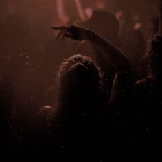 a person standing in front of a crowd holding their hand up to the sky at a concert