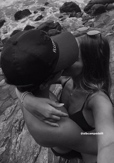 black and white photograph of a woman kissing a man on the beach with rocks in the background