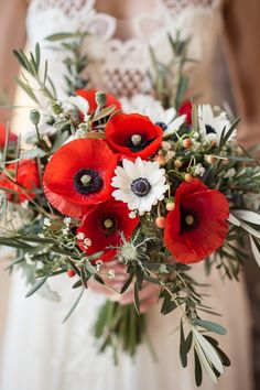 a bride holding a bouquet of red and white flowers with greenery in her hands