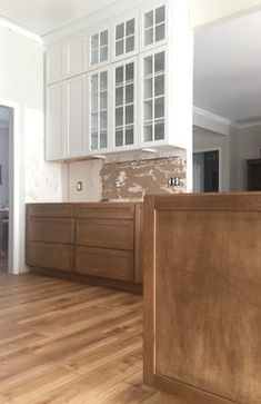 an empty kitchen with wooden floors and white cabinets in the back drop off from the living room