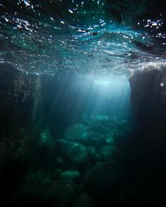 an underwater view of rocks and water with sunlight coming in from the top left corner