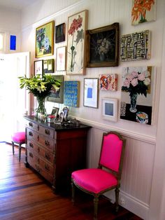 a pink chair sitting in front of a dresser next to a wall with pictures on it