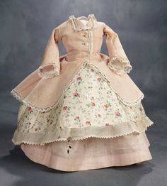 an old fashioned doll is wearing a dress with flowers and ruffles on it