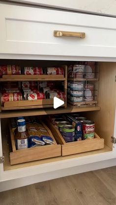 an open cabinet with canned food in the bottom drawer and other items on the bottom shelf