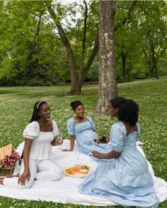 three women are sitting on a blanket in the grass and having a picnic with each other