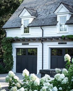 a white house with two black garage doors and some flowers in front of the building