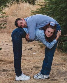 a man and woman standing next to each other in front of some trees with their arms around one another