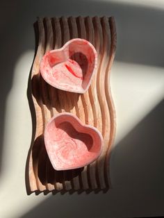 two heart shaped bowls sitting on top of a wooden tray next to a shadow cast wall