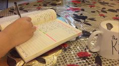 a person writing in a notebook on top of a table with flowers and coffee mugs