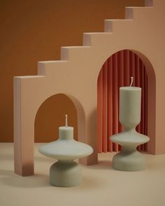 two white candles sitting next to each other in front of a pink and orange wall