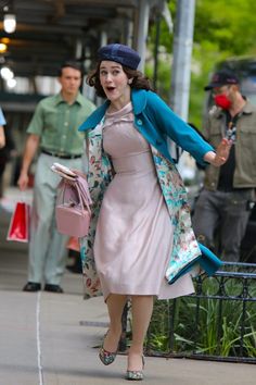 a woman in a pink dress and blue jacket is walking down the street with her purse