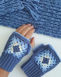 a woman's hand is holding two blue crocheted mitts on top of a white surface