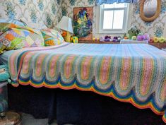 a bedroom with a bed covered in a multicolored crochet blanket and pillows