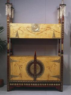 an old wooden bed with decorative carvings on the top and bottom, sitting in front of a potted plant