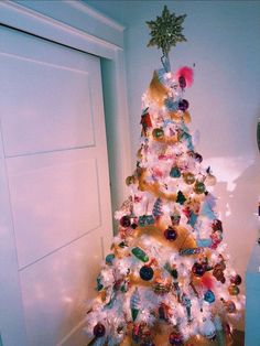 a white christmas tree with ornaments on it in front of a door and a clock